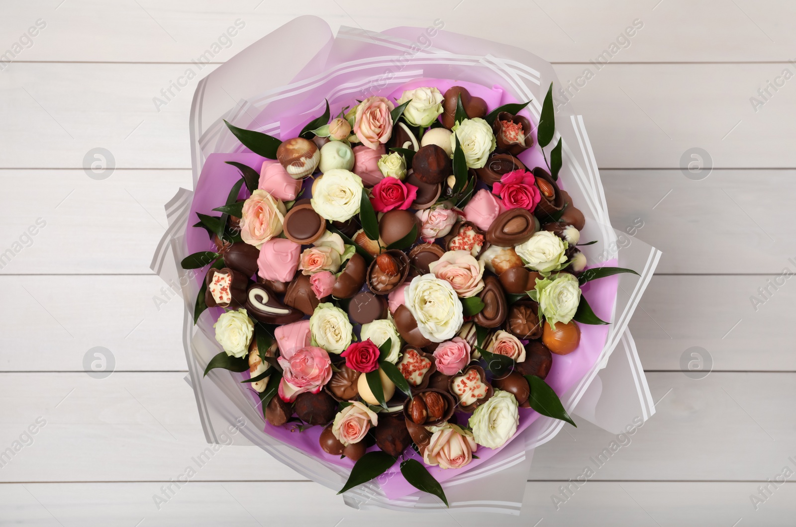 Photo of Beautiful bouquet of flowers and chocolate candies on white wooden background, top view