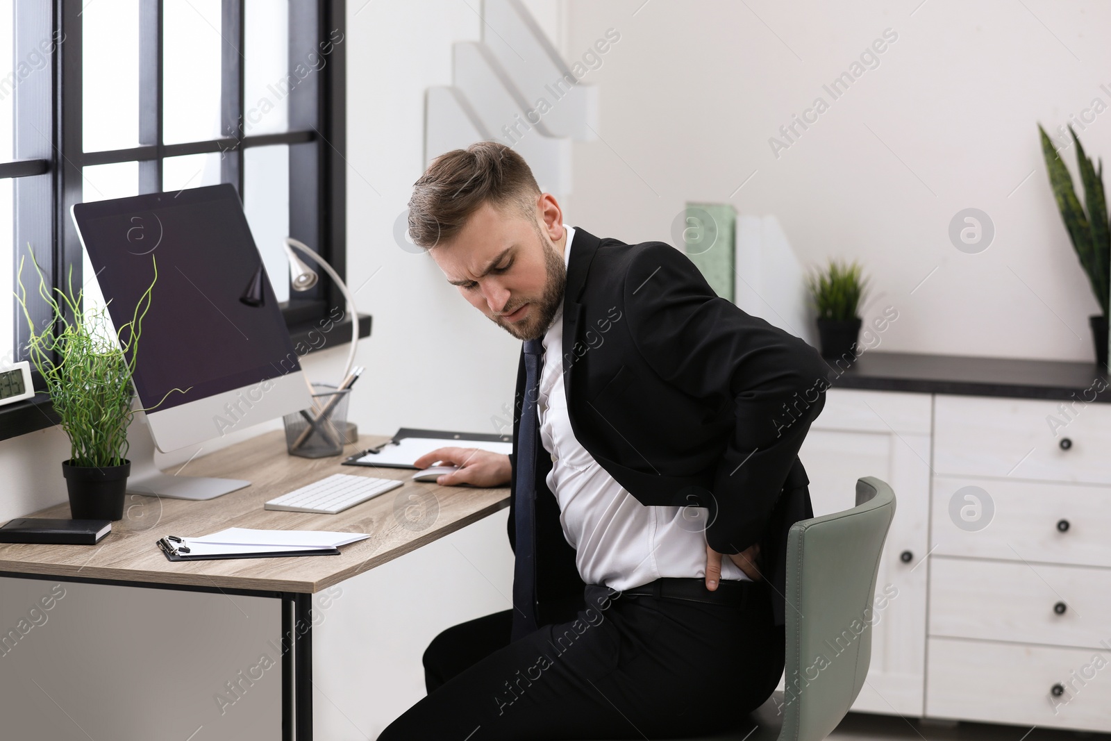 Photo of Businessman suffering from back pain at workplace