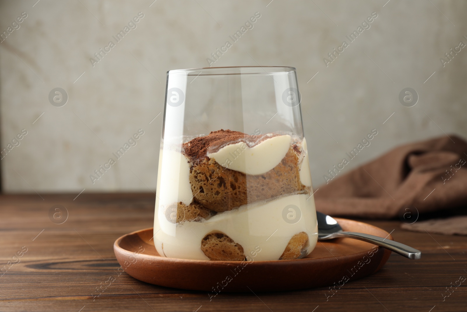 Photo of Delicious tiramisu in glass and spoon on wooden table, closeup