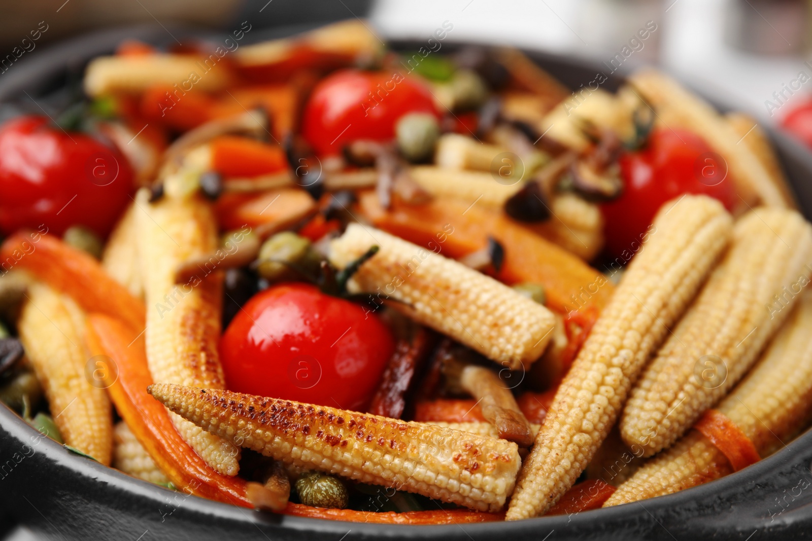 Photo of Tasty roasted baby corn with tomatoes, capers and mushrooms in bowl, closeup