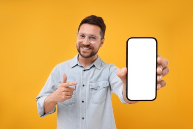 Photo of Handsome man showing smartphone in hand and pointing at it on yellow background
