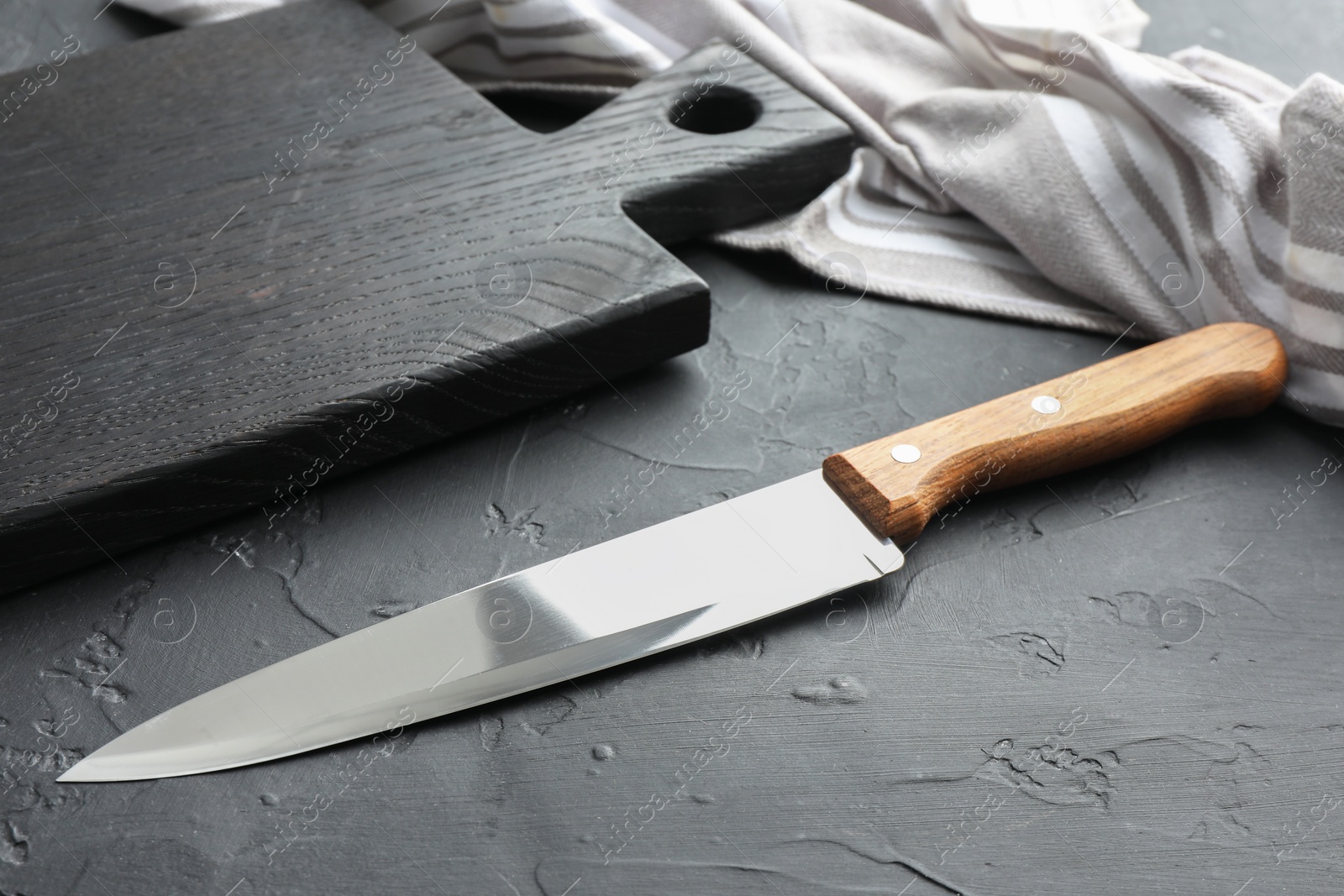 Photo of One sharp knife and board on dark textured table, closeup