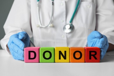 Photo of Doctor making word Donor of wooden cubes with letters at white table, closeup