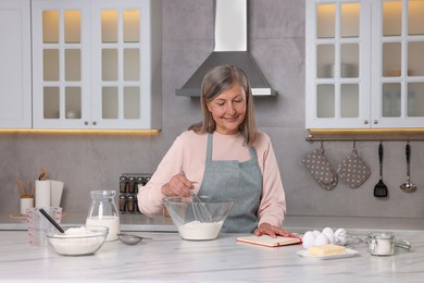 Photo of Senior woman with recipe book cooking in kitchen