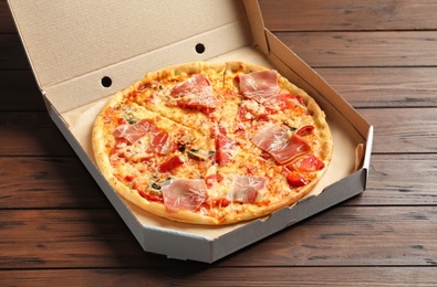 Photo of Carton box with delicious pizza on wooden background