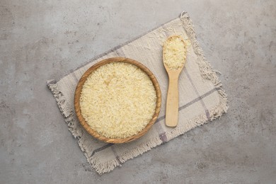 Bowl and spoon of raw rice on grey table, top view