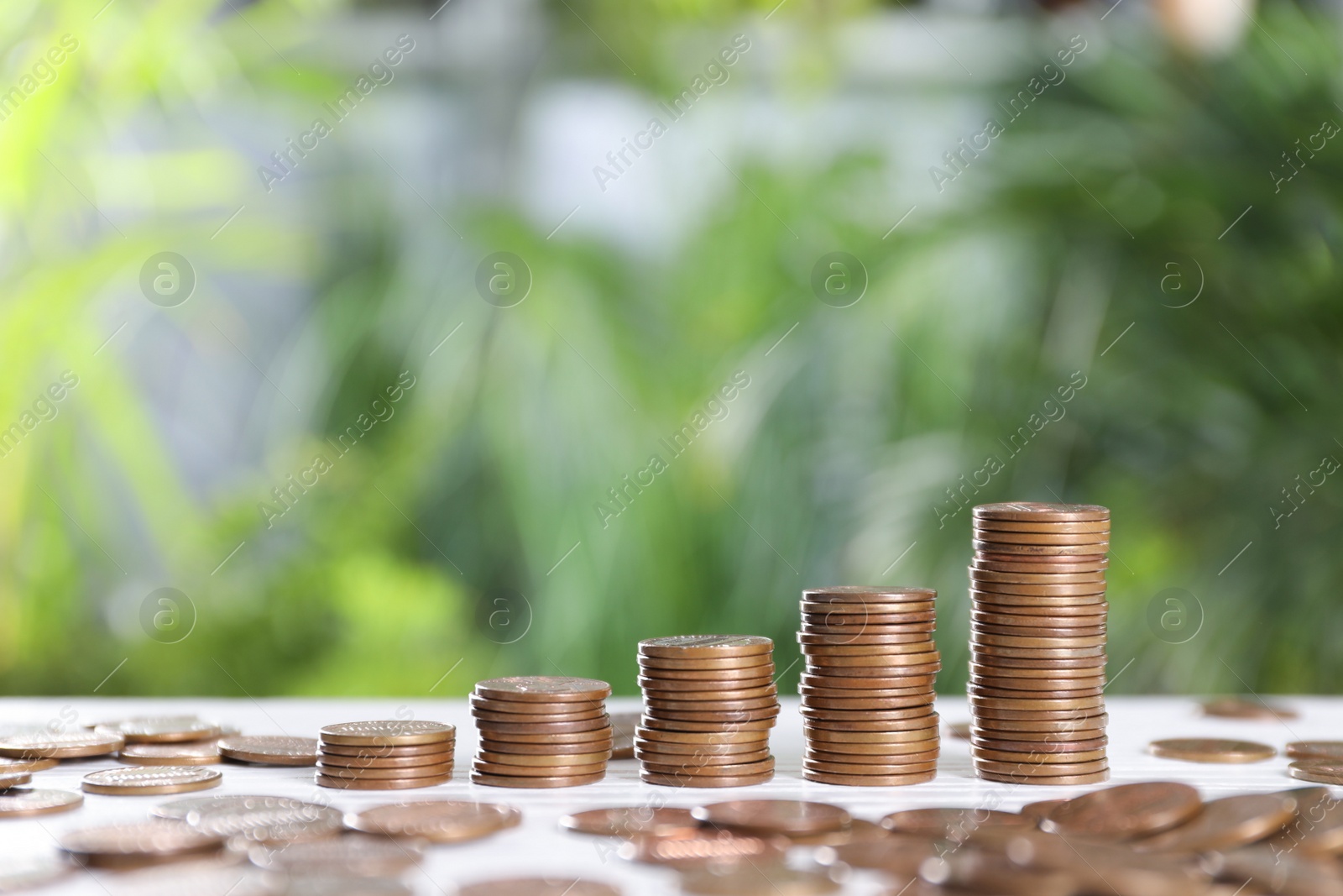 Photo of Many metal coins on white table against blurred green background. Space for text