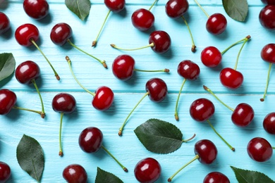 Photo of Sweet juicy cherries on light blue wooden table, flat lay