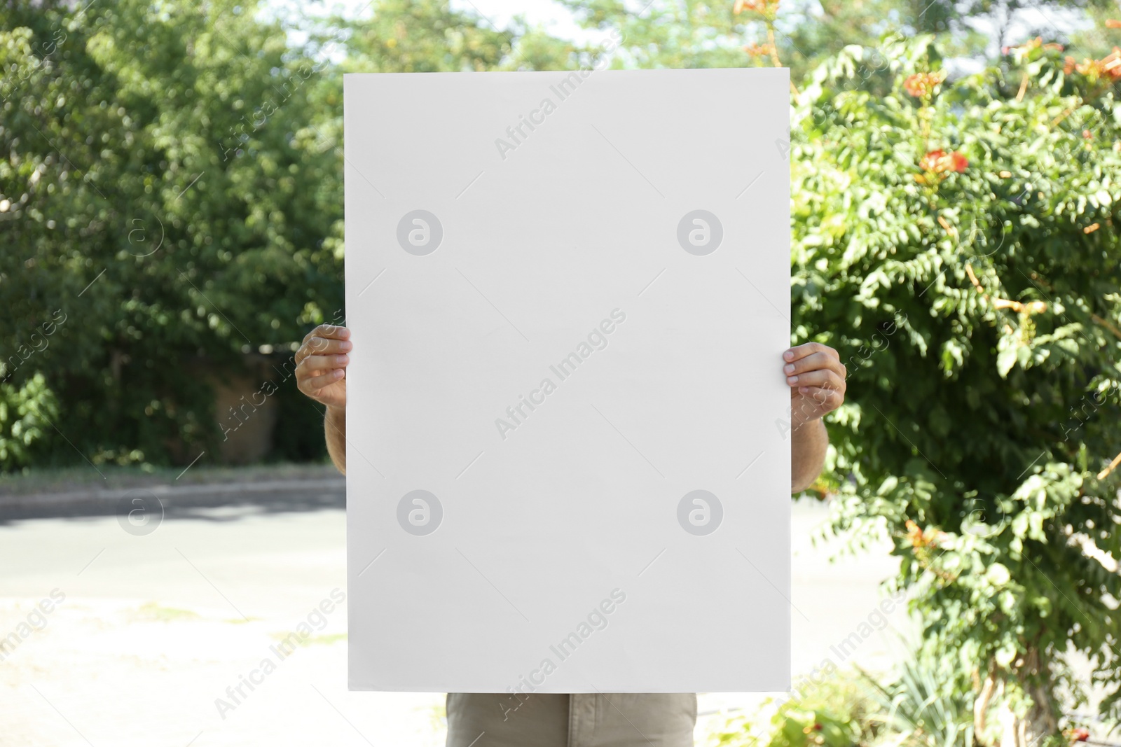 Photo of Man holding white empty poster outdoors. Space for design