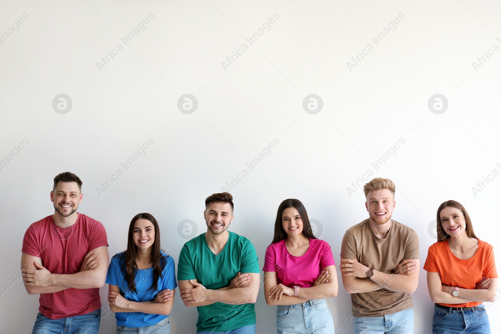 Photo of Group of happy people posing near light wall, space for text