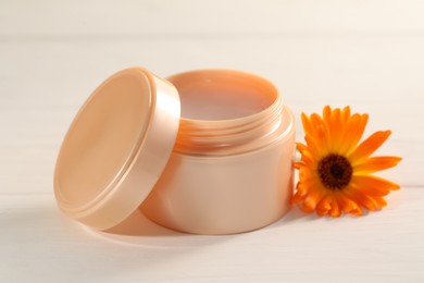 Photo of Jar of cream and beautiful calendula flower on white wooden table, closeup