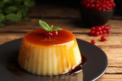 Plate of delicious caramel pudding with red currants and mint on wooden table, closeup