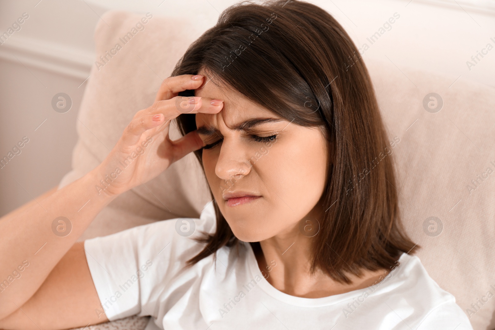 Photo of Young woman suffering from migraine on sofa at home