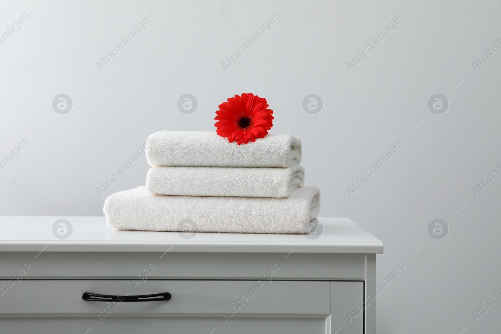 Photo of Stack of fresh towels with flower on cabinet against white background. Space for text