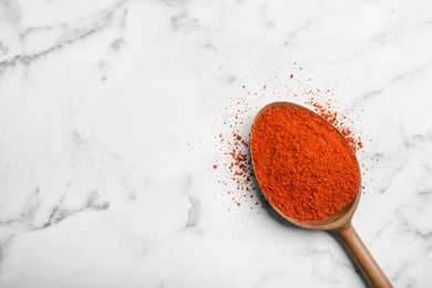 Photo of Powdered chili pepper in wooden spoon and space for text on marble background, top view