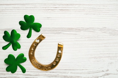 Golden horseshoe and decorative clover leaves on white wooden table, flat lay with space for text. Saint Patrick's Day celebration