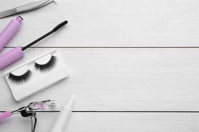 Flat lay composition with false eyelashes and tools on white wooden table. Space for text