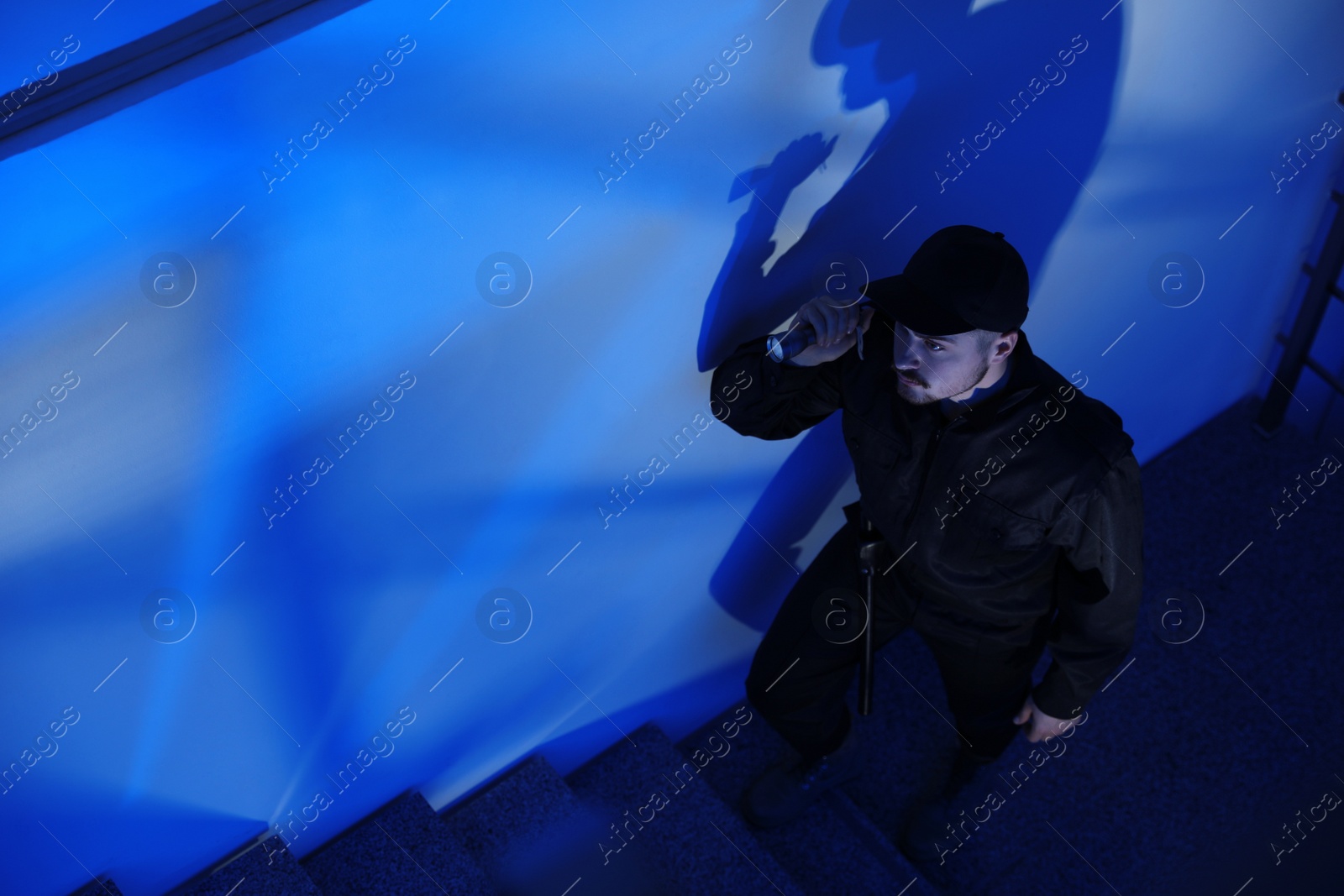 Photo of Male security guard with flashlight going up stairs in darkness