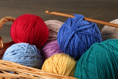 Photo of Clews of colorful knitting threads and crochet hook in wicker basket, closeup