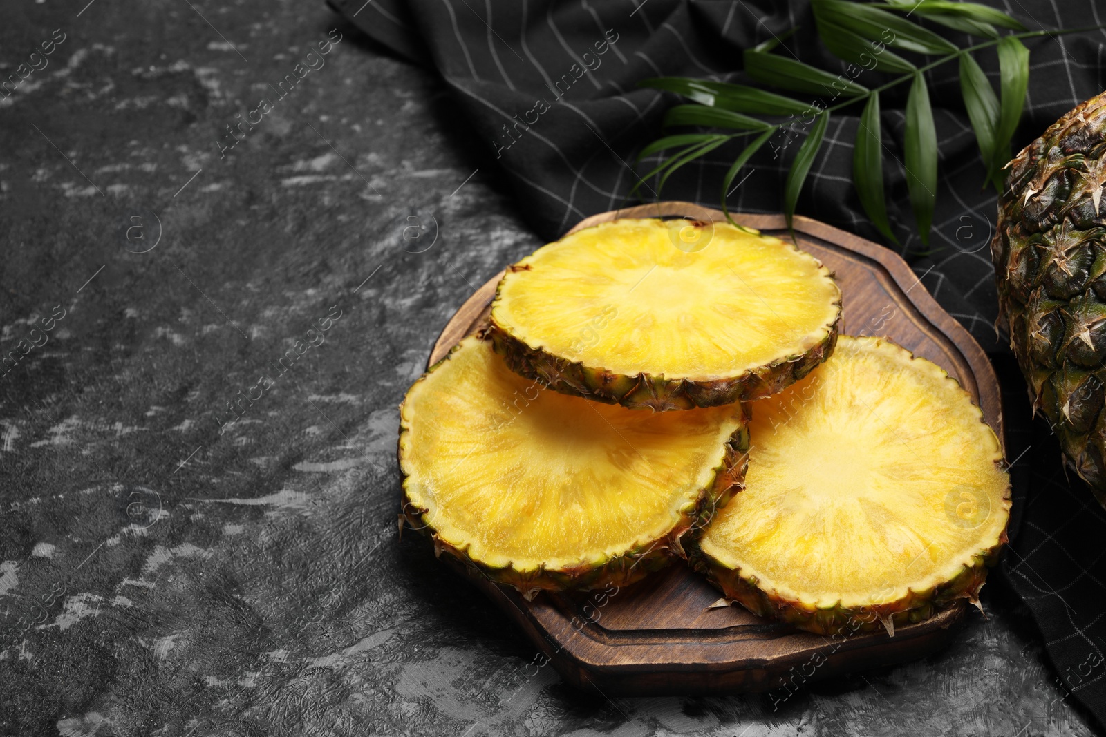 Photo of Slices of tasty ripe pineapple on black textured table, space for text