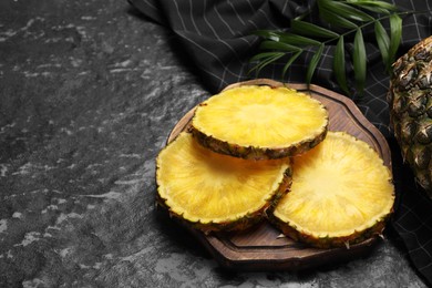 Slices of tasty ripe pineapple on black textured table, space for text