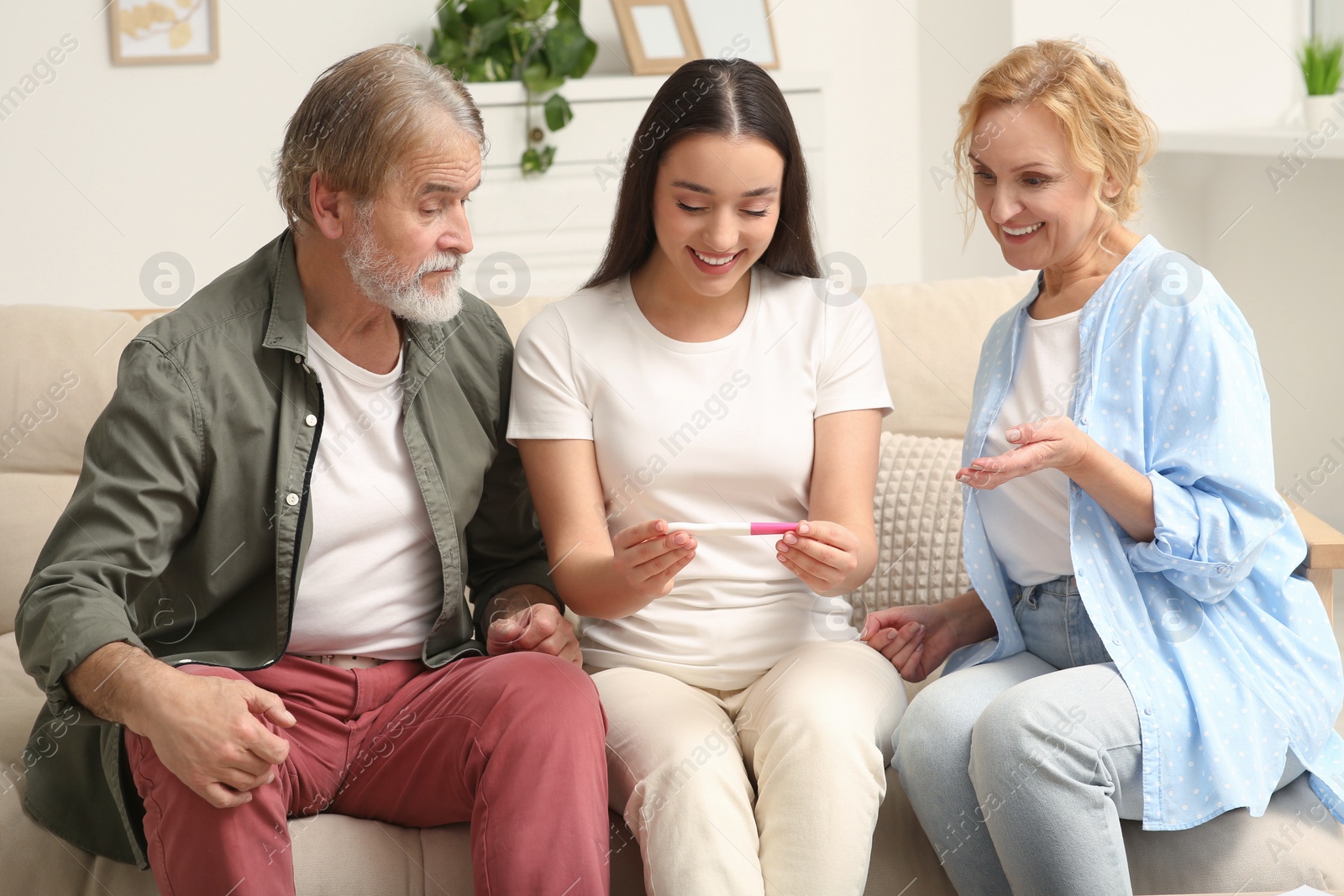 Photo of Happy pregnant woman showing her parents pregnancy test at home . Grandparents' reaction to future grandson