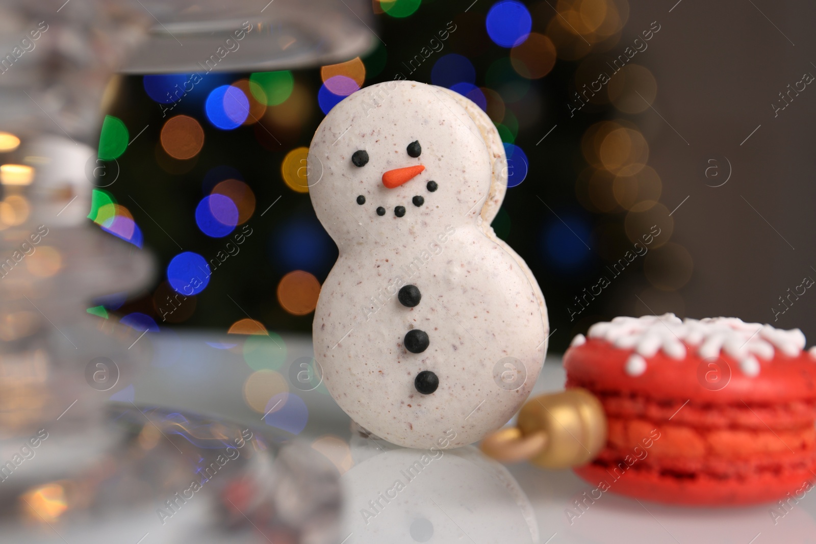 Photo of Beautifully decorated Christmas macarons on white stand against blurred festive lights, closeup