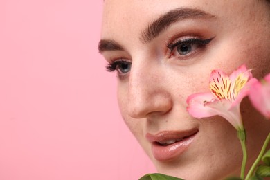 Beautiful woman with fake freckles and flowers on pink background, closeup. Space for text