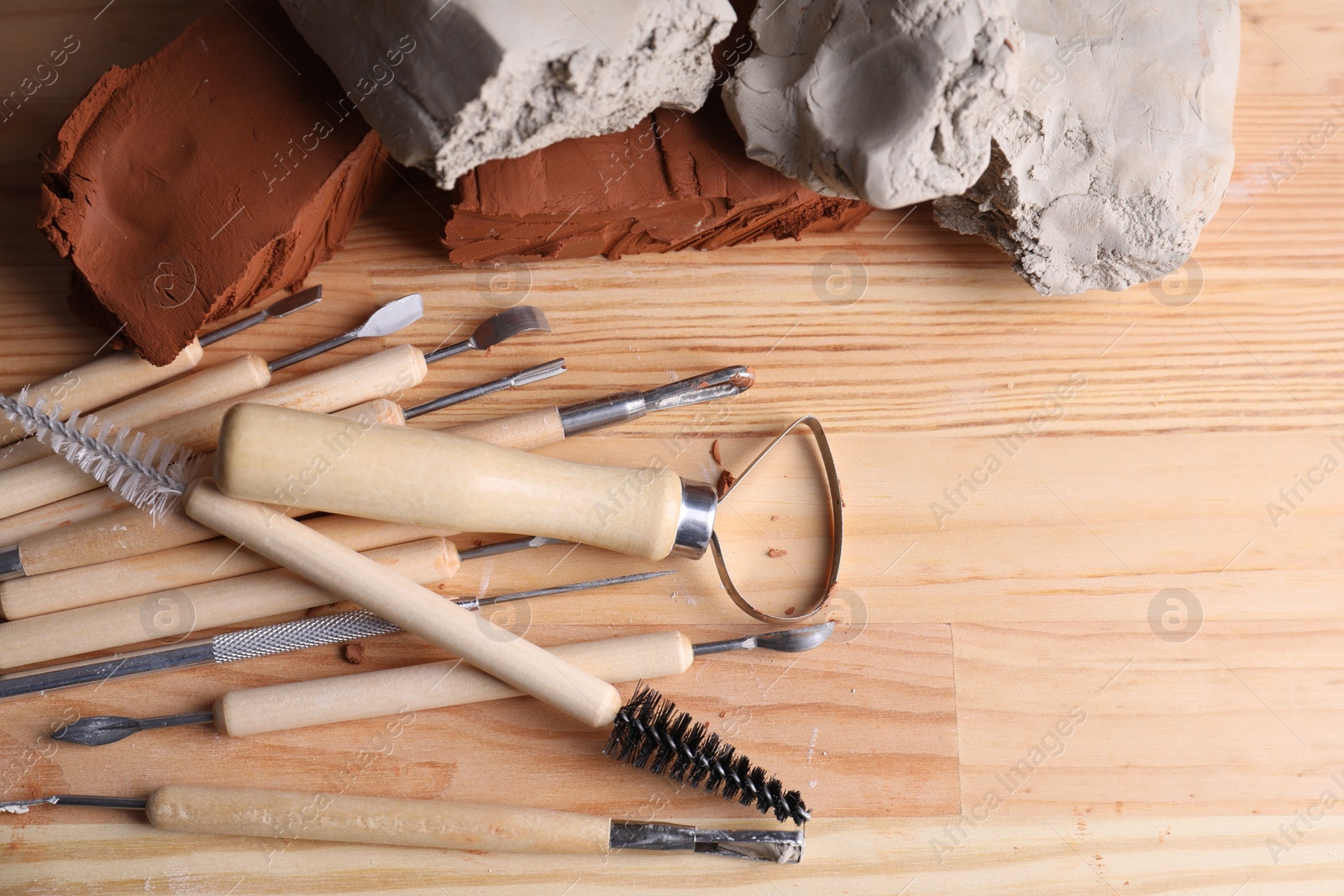 Photo of Clay and set of modeling tools on wooden table, flat lay