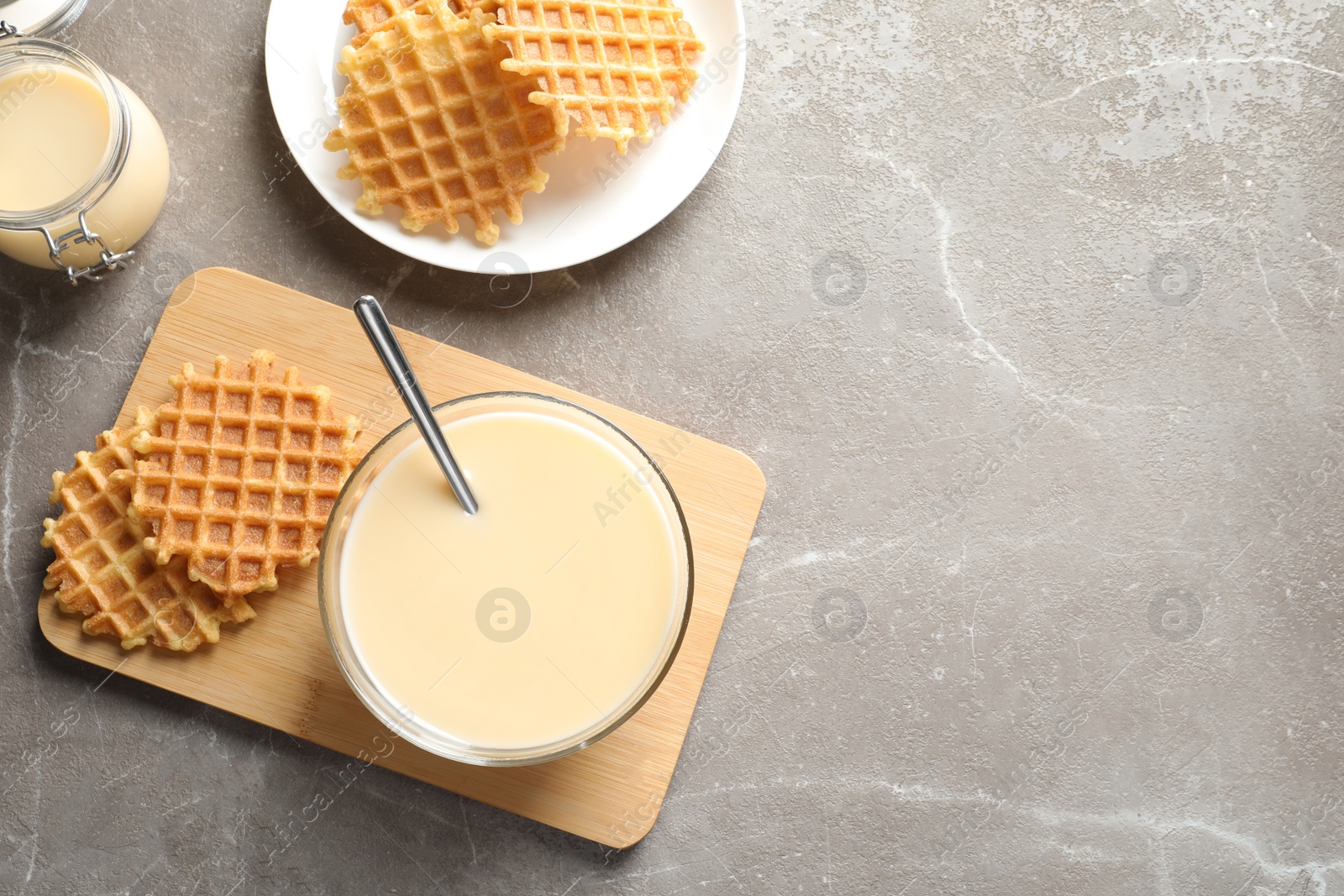 Photo of Bowl of condensed milk and waffles served on grey table, top view with space for text. Dairy products