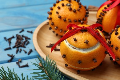 Photo of Pomander balls made of tangerines with cloves and fir branch on light blue wooden table, closeup. Space for text