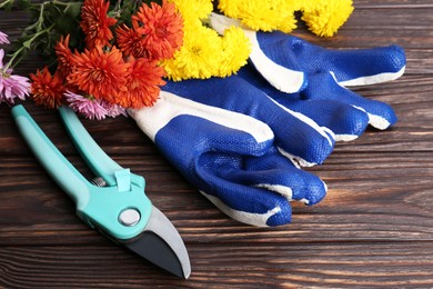 Photo of Gardening gloves, pruner and flowers on wooden table, closeup
