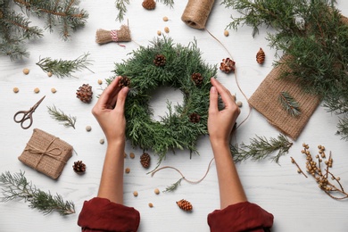 Photo of Florist making beautiful Christmas wreath with pine cones at white wooden table, top view