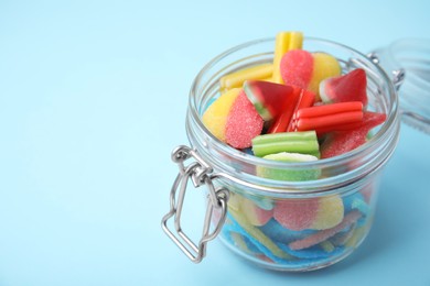 Photo of Tasty colorful jelly candies in glass jar on light blue background, closeup. Space for text
