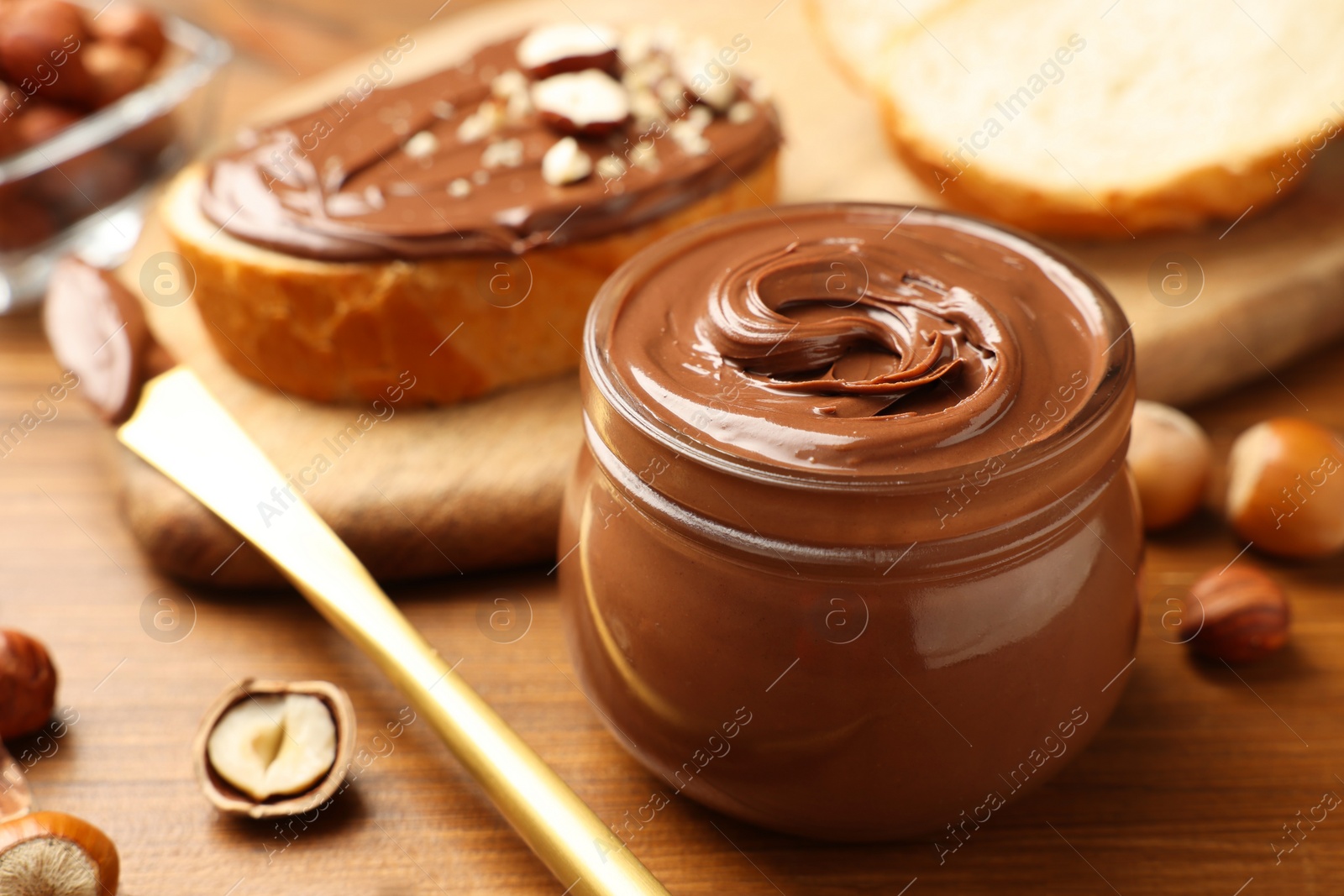 Photo of Glass jar with tasty chocolate hazelnut spread and nuts on wooden table, closeup