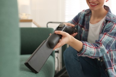 Photo of Young woman vacuuming sofa in living room, closeup