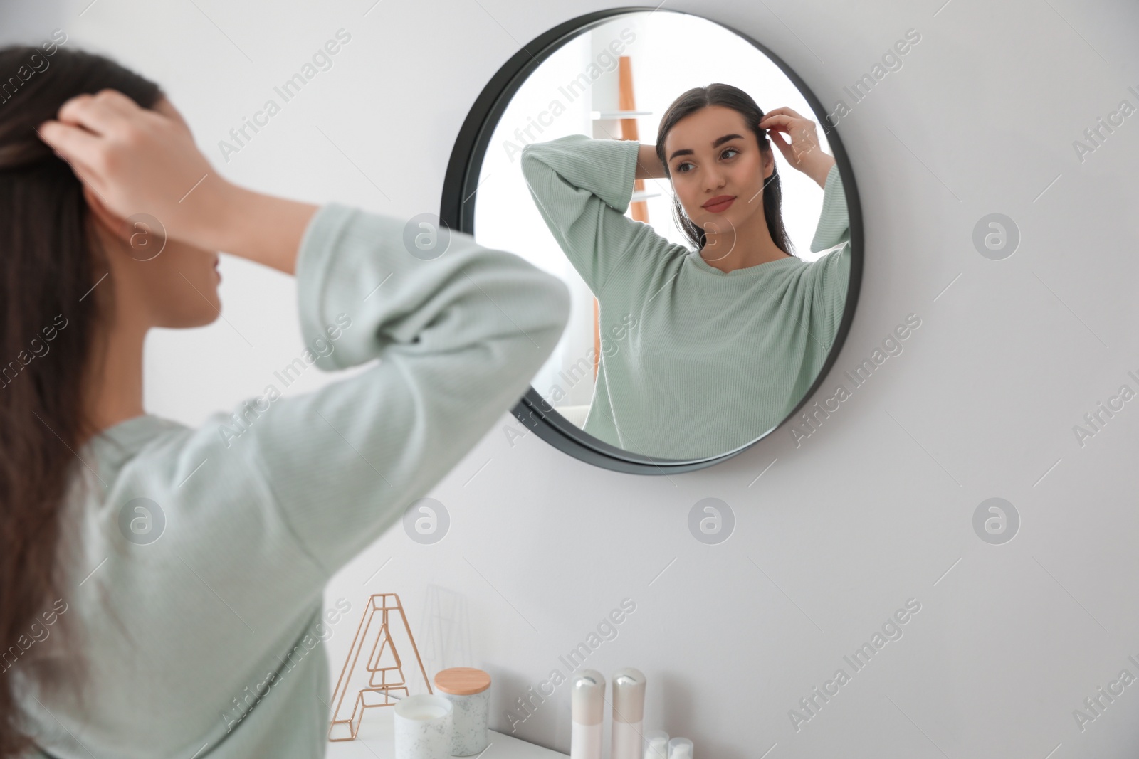 Photo of Young woman doing hair near mirror at home. Morning routine