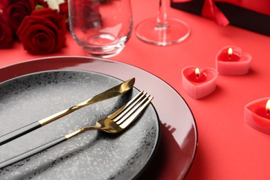 Photo of Place setting with heart shaped candles, gift box and bouquet of roses on red table, closeup. Romantic dinner