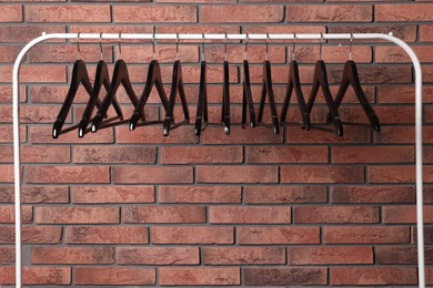 Photo of Black clothes hangers on rack near red brick wall. Space for text