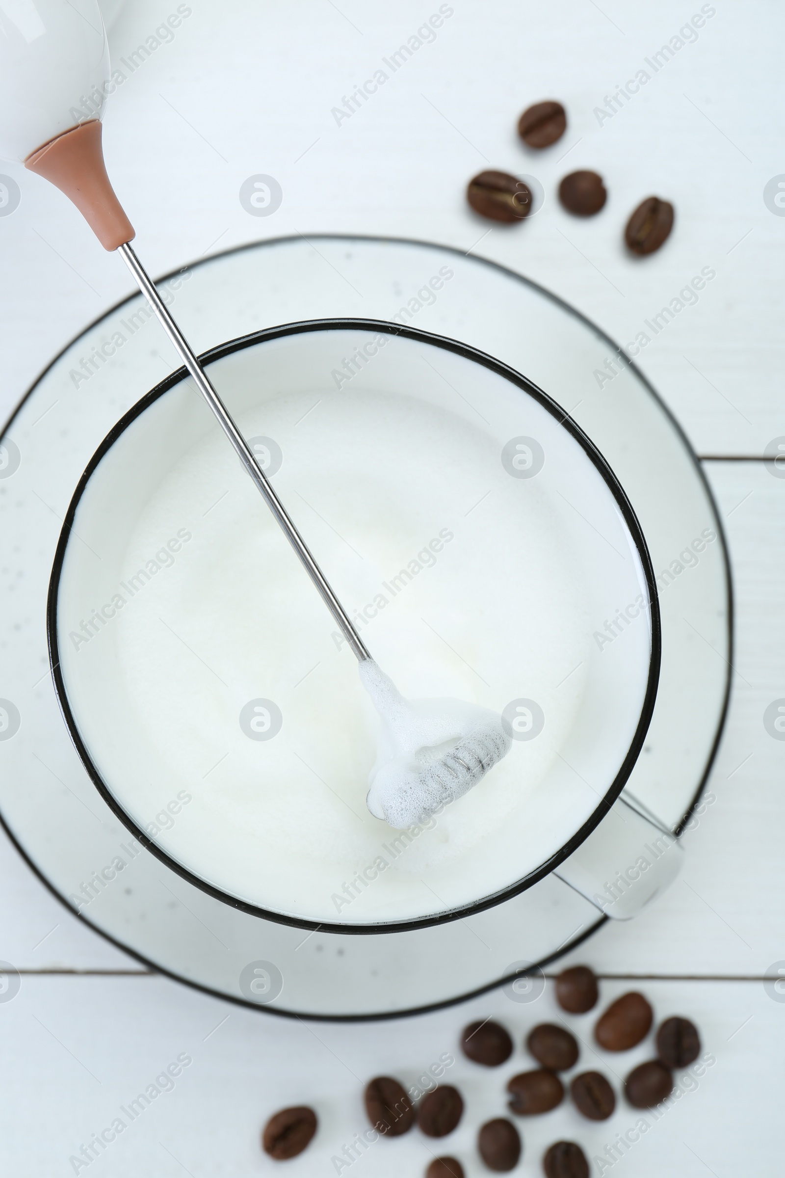 Photo of Mini mixer (milk frother), whipped milk and coffee beans on white wooden table, flat lay