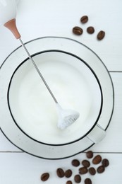 Mini mixer (milk frother), whipped milk and coffee beans on white wooden table, flat lay