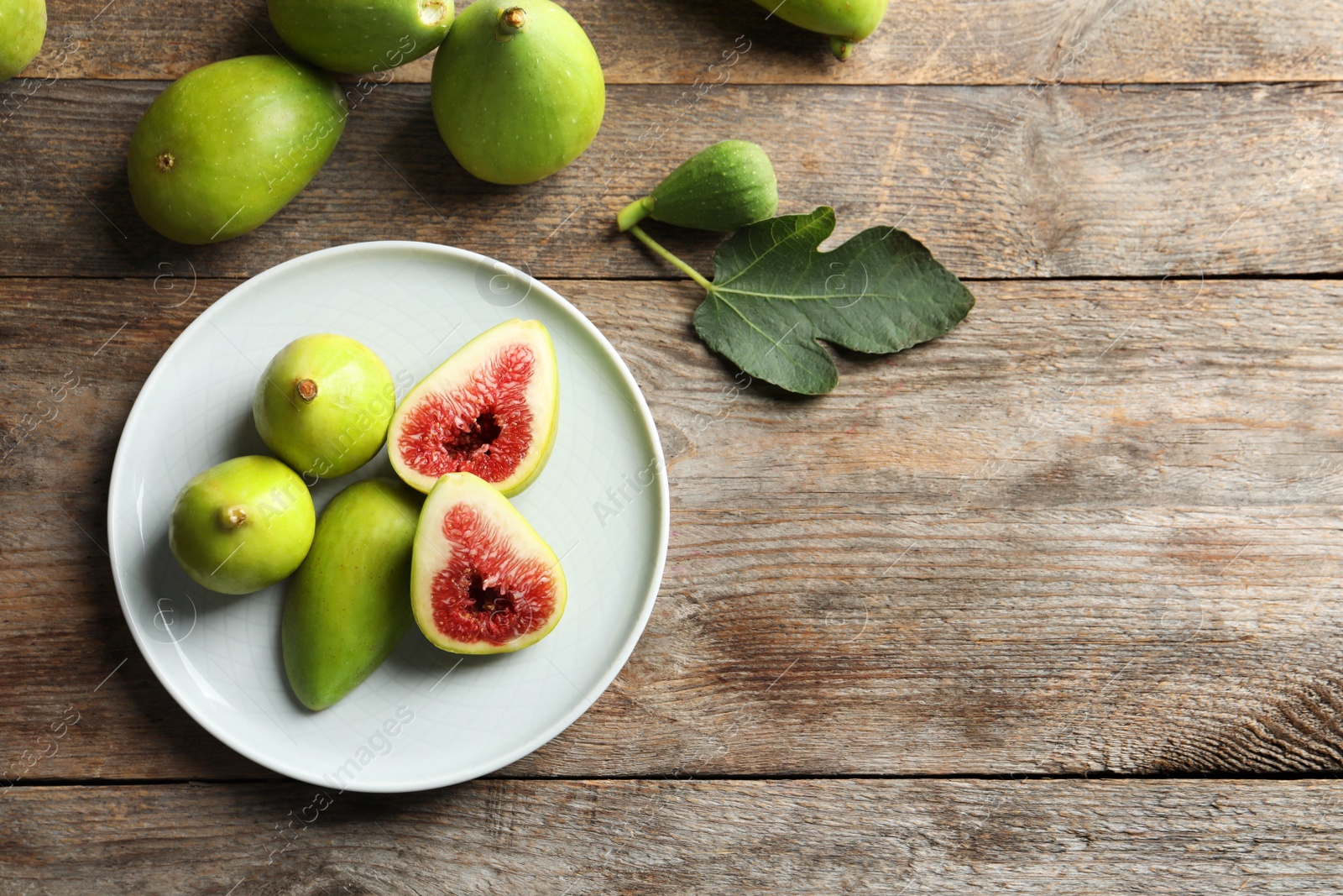 Photo of Plate with fresh ripe figs on wooden background, top view. Space for text