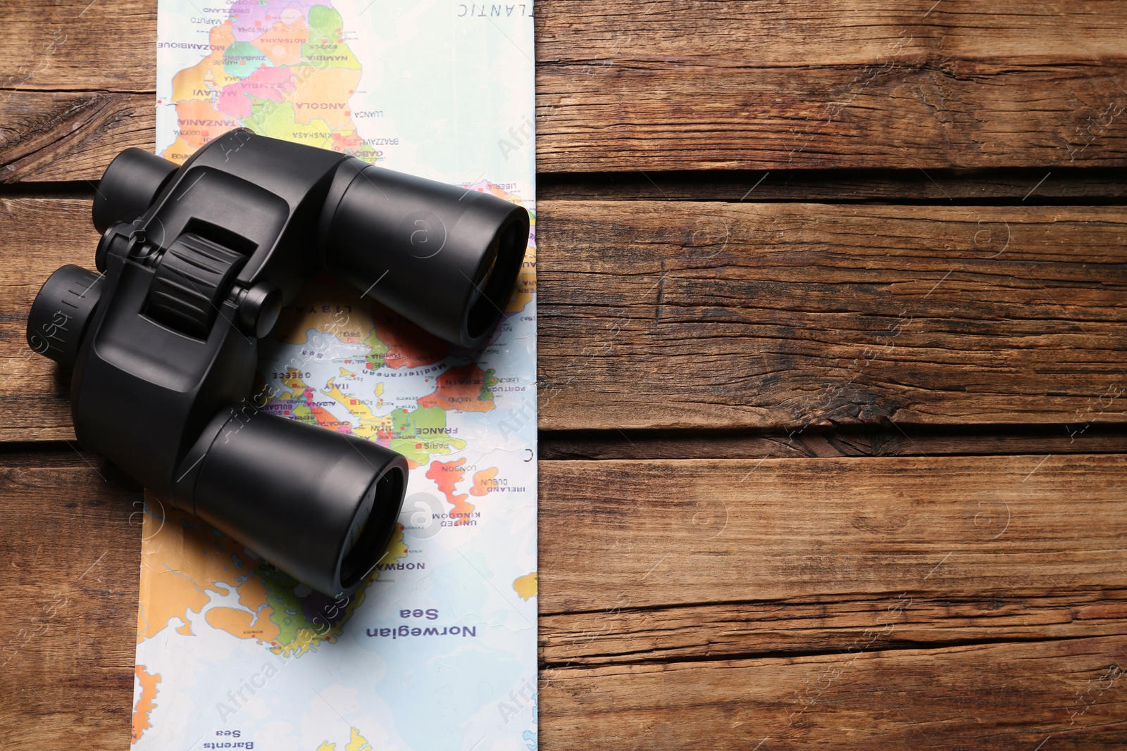 Photo of Modern binoculars and map on wooden table, top view. Space for text