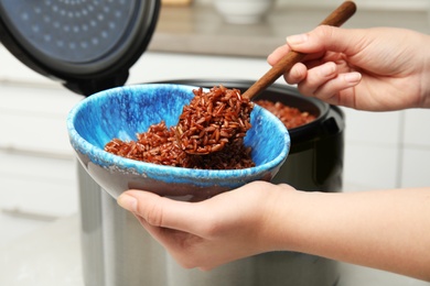 Woman putting delicious brown rice into bowl from multi cooker, closeup