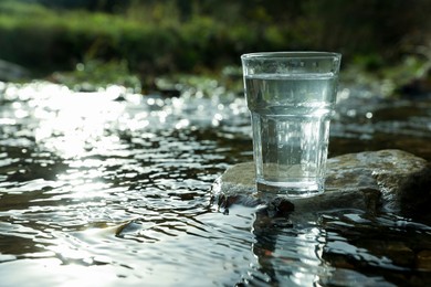 Glass of fresh water on stone near river outdoors. Space for text