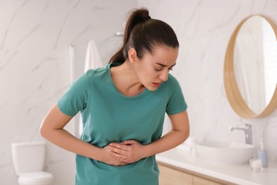 Photo of Young woman suffering from stomach ache in bathroom. Food poisoning