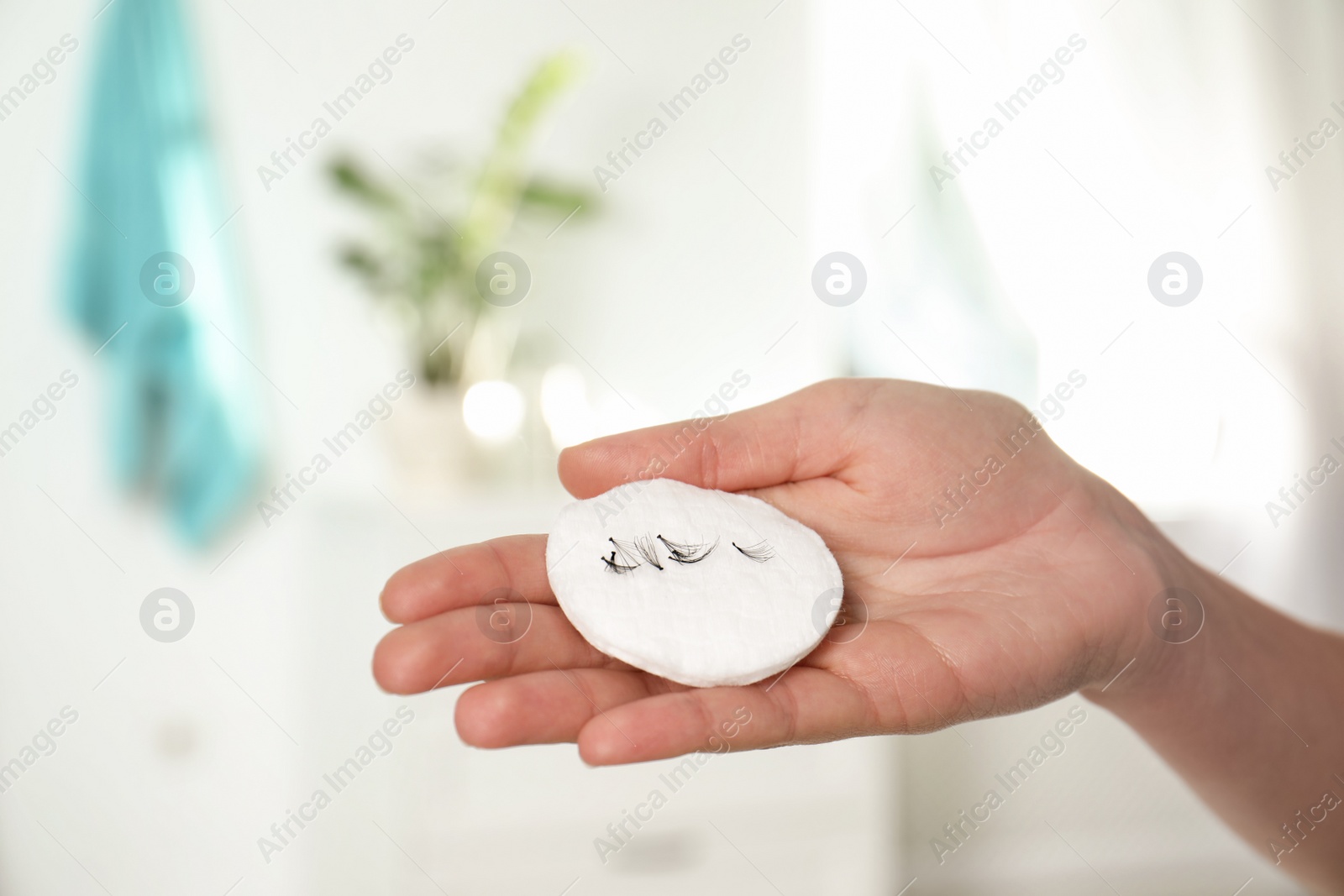 Photo of Woman holding cotton pad with fallen eyelashes indoors, closeup of hand