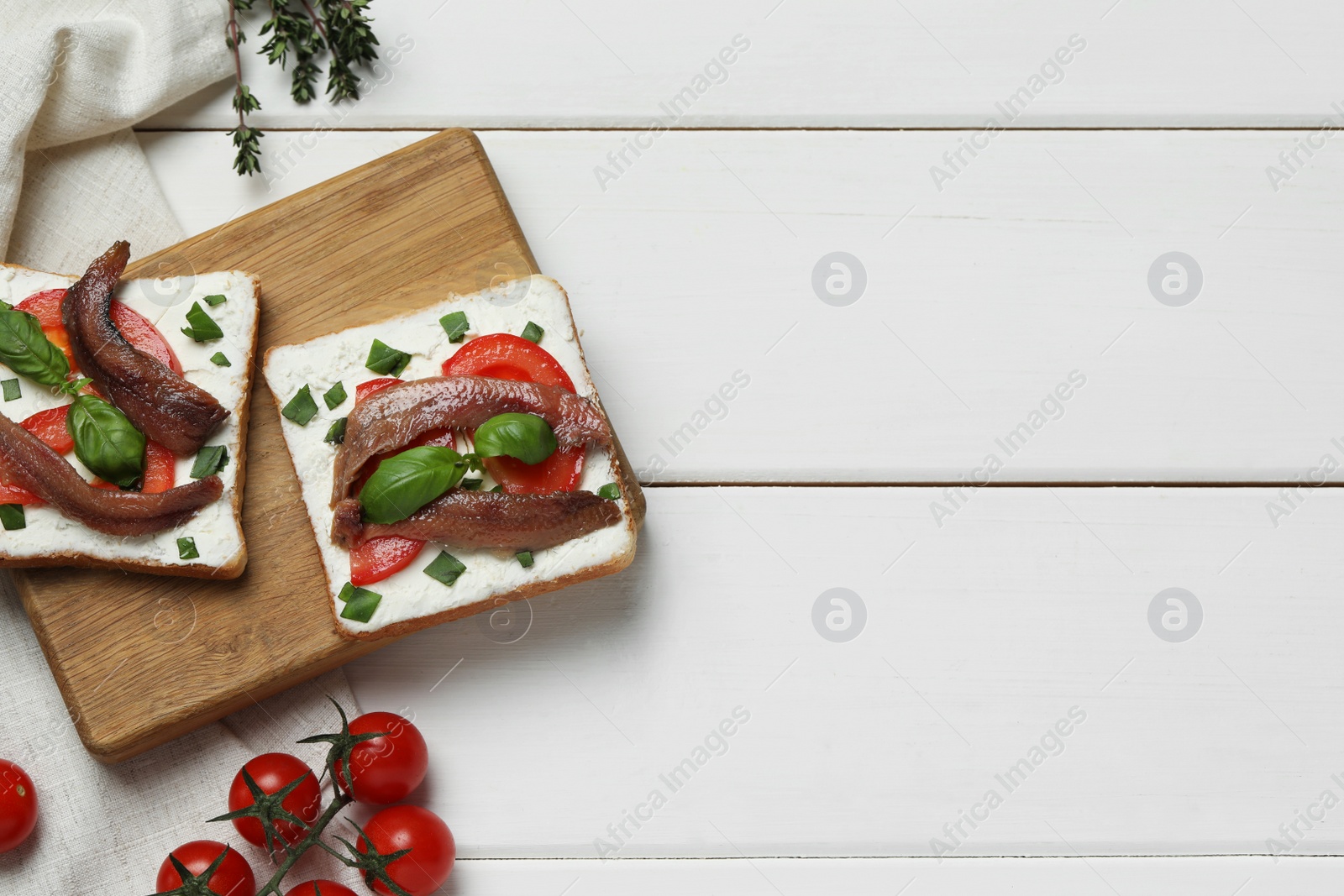 Photo of Delicious sandwiches with cream cheese, anchovies, tomatoes and basil on white wooden table, flat lay. Space for text