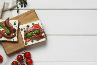 Delicious sandwiches with cream cheese, anchovies, tomatoes and basil on white wooden table, flat lay. Space for text