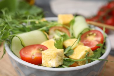 Photo of Bowl of tasty salad with tofu and vegetables on wooden board, closeup